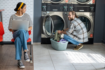 Freelancer woman using laptop while man doing laundry at laundromat
