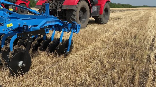 Rear view of a large tractor with a disk harrow plow standing in a field.