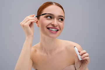 Young female model applying black mascara to lashes