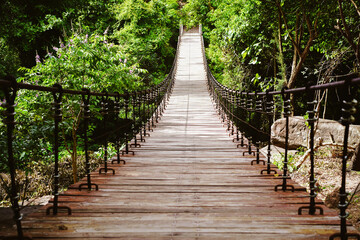 Obraz premium Wooden footbridge and nature jungle. Wooden walking swing bridge, Wooden pathway in tropical forest, a suspension bridge across Tat Ton Waterfall at Tat Ton National Park, Chaiyaphum, Thailand.