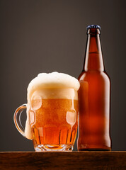 A bottle of beer and a glass of beer on a dark background.