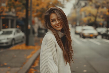 Fototapeta premium Stylish woman in white sweater walking on city street with autumn trees and fallen leaves