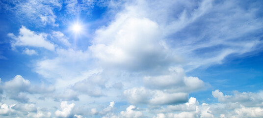 Blue sky with clouds and bright sun. Wide photo.