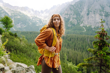 Smiling female with backpack on hike in nature. Beautiful woman hiker standing on mountain trail...