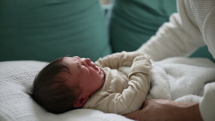 Close-up of a newborn baby crying, lying on a soft blanket on a sofa, with a caring grandmother nearby, capturing the moments of early infancy and family interaction