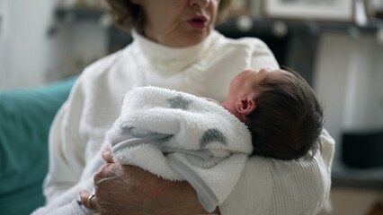 Grandmother holding her newborn grandchild in a cozy blanket, over her shoulder, in a home setting, emphasizing the nurturing bond, care, and warmth between the two generations