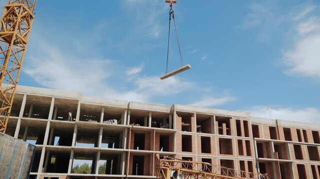 Construction Site with Crane Lifting Concrete Slab. A dynamic view of a construction site where a crane is lifting a concrete slab towards the upper levels of a building under construction.