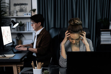 Businesswoman working on desk with stretching arm up and down manner with body health ache of strain overwork while coworker trading stock market on website on pc at late over night time. Infobahn.