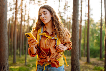 Young woman using mobile application to navigate in autumn forest. Happy tourist trying to find...