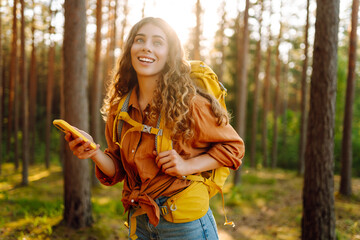 Young woman using mobile application to navigate in autumn forest. Happy tourist trying to find...