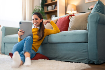 A cheerful caucasian woman enjoys a relaxed video chat on her tablet, with a coffee cup in hand,...