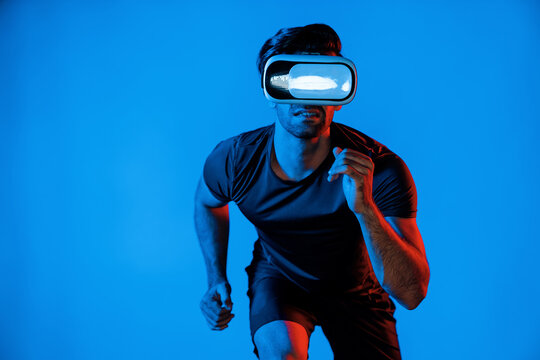 Caucasian smart man jogging while wearing VR goggle with neon light. Happy person with casual cloth running or exercising while using virtual reality headset. Innovation technology concept. Deviation.