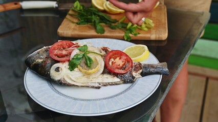Delicious grilled fish with lemon, tomato, and herbs on a plate ready to serve at outdoor barbecue