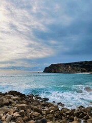 Shoreline with cloudy sky and beautiful turquoise water, hidden peaceful beach in Portugal.