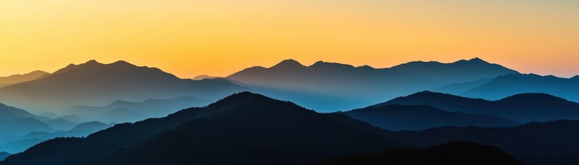 Obraz premium Breathtaking sunrise over misty mountains, casting silhouettes in blue and orange hues, perfect for nature, travel, and adventure themes.