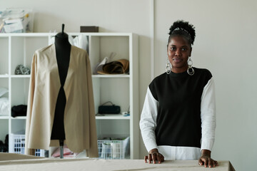 Young successful female couturier in casual pullover and stylish earrings looking at camera while...