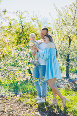 Obraz premium A young married couple with a small son in a blooming garden. A happy family couple with a child on a walk in the garden.