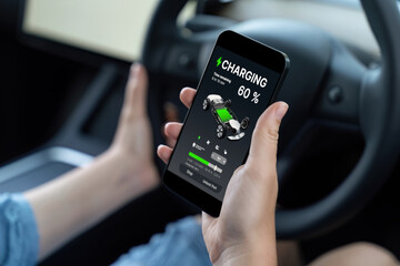 Holiday vacation road trip with environmental-friendly car concept. Eco-conscious woman on driver seat checking EV car's battery status display on smartphone during car travel. Perpetual