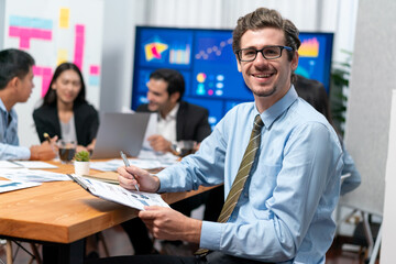 Portrait of businessman or analyst looking at camera with his colleague analyzing data analysis in dynamic business strategy investment planning meeting. Meticulous