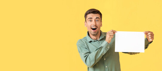 Surprised young man with blank paper sheet on color background