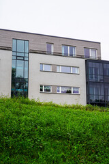 Grey building with many windows. Dark green grass hill in the front. Wooden panels details. Summer daytime. Tree foliage on the right. Tallinn, Estonia, Europe. July 2024
