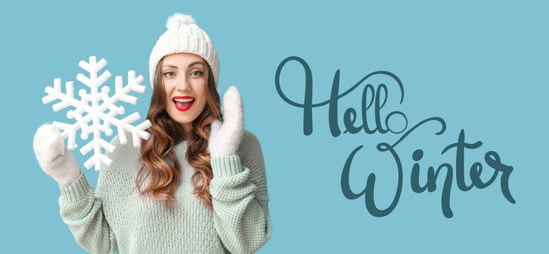 Happy woman in warm clothes holding big snowflake on blue background. Hello, winter