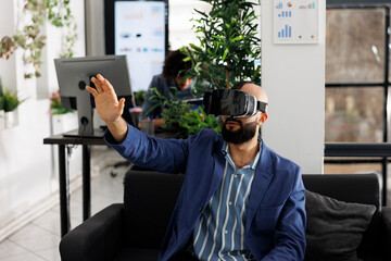 Entrepreneur using vr glasses for market research and analysis while working in business office. Project manager wearing virtual reality headset while sitting on couch in coworking space