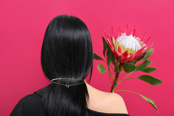 Naklejka premium Beautiful young woman wearing golden necklace with protea flower near red wall, back view
