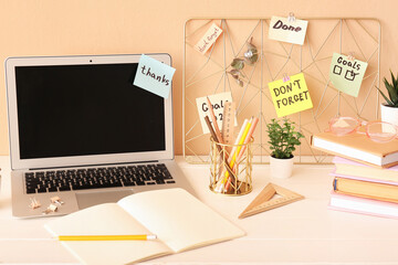 Laptop with sticky notes and stationery on table near beige wall