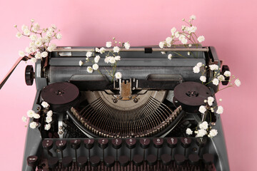 Vintage typewriter with gypsophila flowers on pink background, closeup