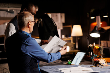 Fototapeta premium Tailors checking fashion sketches, comparing different clothing combinations in atelier shop. Master dressmaker and african american apprentice working on clothing adjustments for upcoming collection
