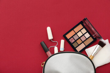 Lady's cosmetic bag with menstrual pad, tampons and makeup products on red background