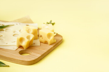 Board with pieces of Swiss cheese on yellow background
