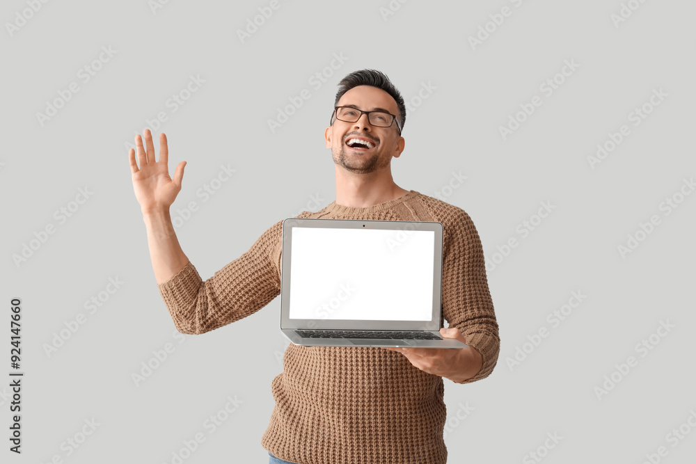 Wall mural Happy young man with laptop on light background