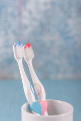 There is a heart pattern on the toothbrush handle. Two toothbrushes in ceramic mug on blue...