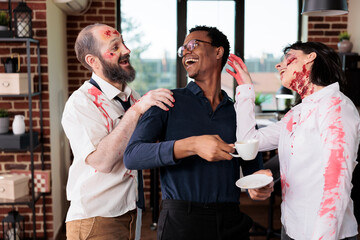 Actors portraying bloody zombie role in horror movie laughing with BIPOC director on office building set. Filmmaker and thriller slasher film extras having fun between scene takes © DC Studio