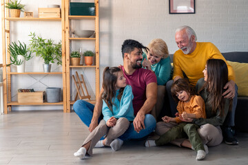 A joyful family of diverse ages relaxes on a sofa and floor, with casual attire, sharing smiles in...