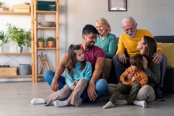 A joyful family spans generations, gathers in cozy living room for portrait. Adults and children...