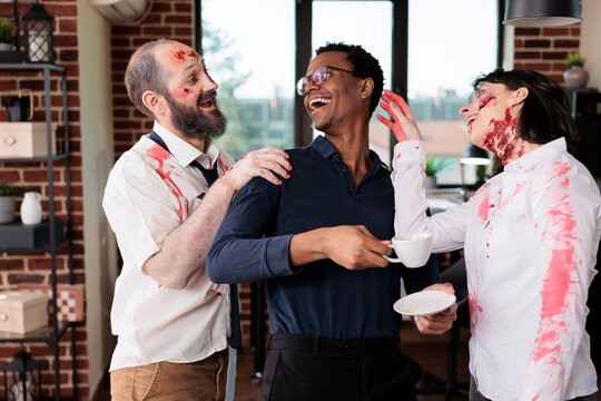 Actors portraying bloody zombie role in horror movie laughing with BIPOC director on office building set. Filmmaker and thriller slasher film extras having fun between scene takes