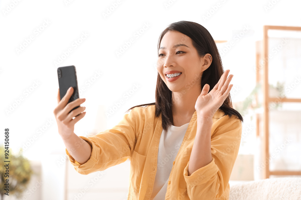 Poster beautiful young asian woman with mobile phone waving hand at home