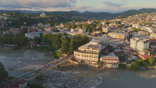 Fly over Kutaisi white bridge and old town in warm sunset lights. Aerial view of river Rioni in Kutaisi, Georgia