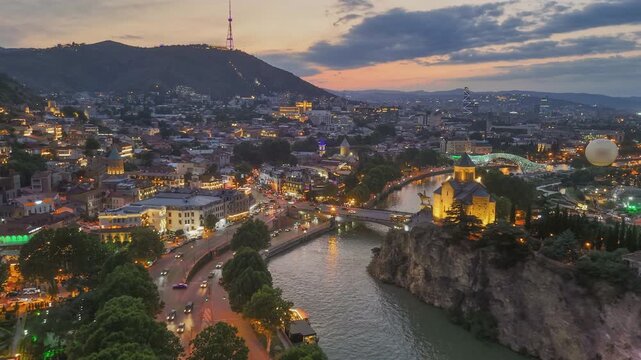 Aerial shot of beautiful evening Tbilisi with susnet sky background, Georgia. Fly over Kura river and Tbilisi old town