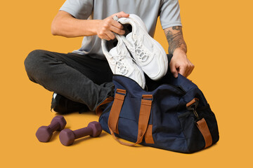 Young man with sports bag on yellow background