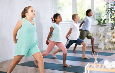 Obraz premium Young girl in group of multiethnic children doing pilates in studio