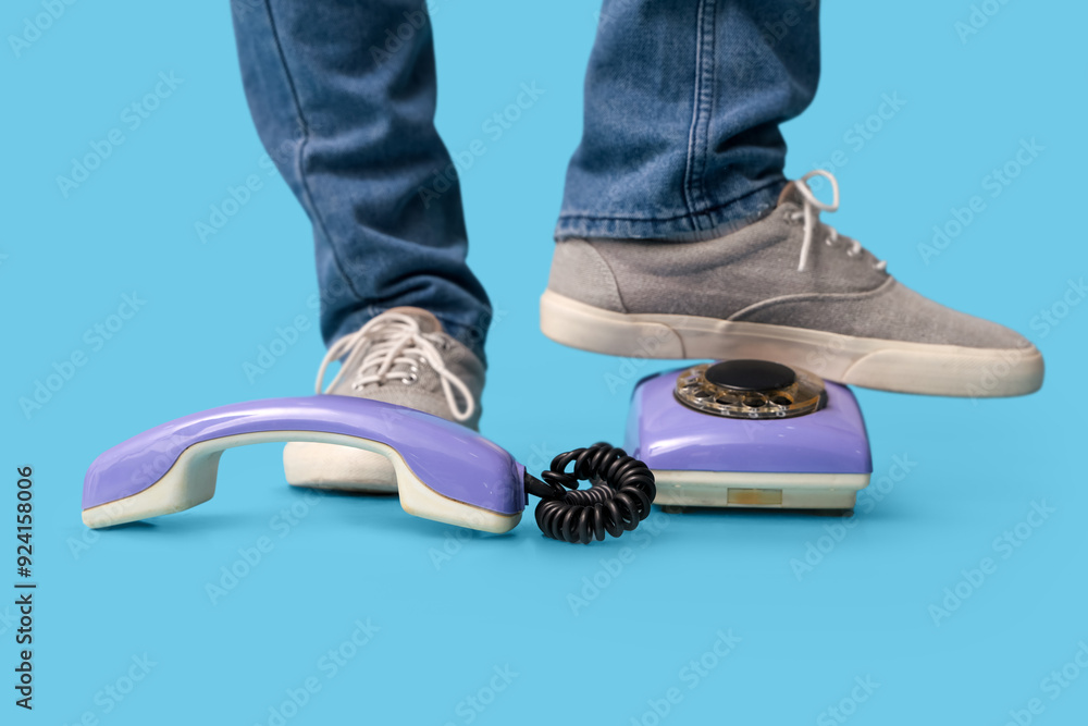 Wall mural legs of young man in grey stylish sneakers and telephone on blue background