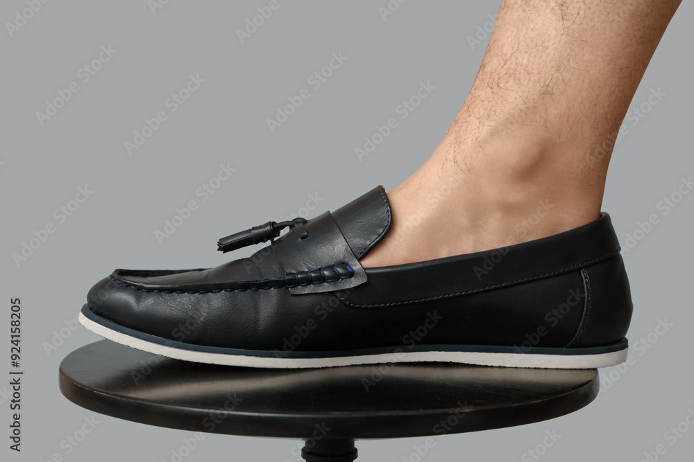 Wall mural leg of young man in black stylish shoe on chair against grey background