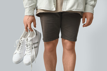 Young man with white stylish sneakers on grey background