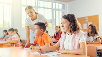 Portrait of assiduous focused tween girl sitting at desk with pen and notebook at lesson at school