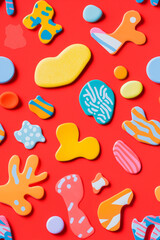A seamless pattern of colorful, organic shapes against a vibrant red background. The abstract design features playful, irregular forms in various colors, creating a lively and dynamic composition.