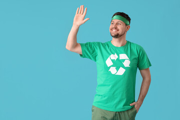 Happy young man in t-shirt with recycling logo waving hand on blue background. Ecology concept